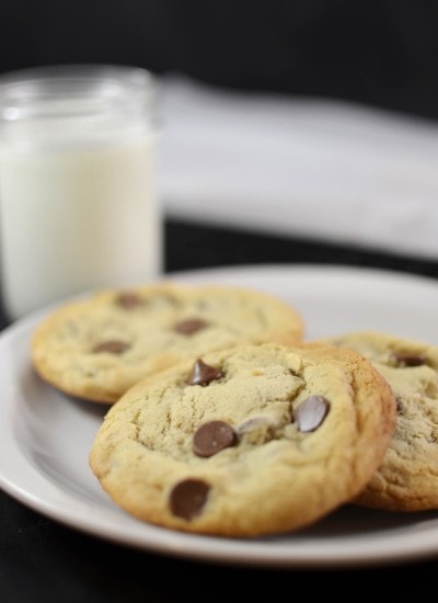 Angled view of chocolate chip cookies on a white plate with milk in the background.