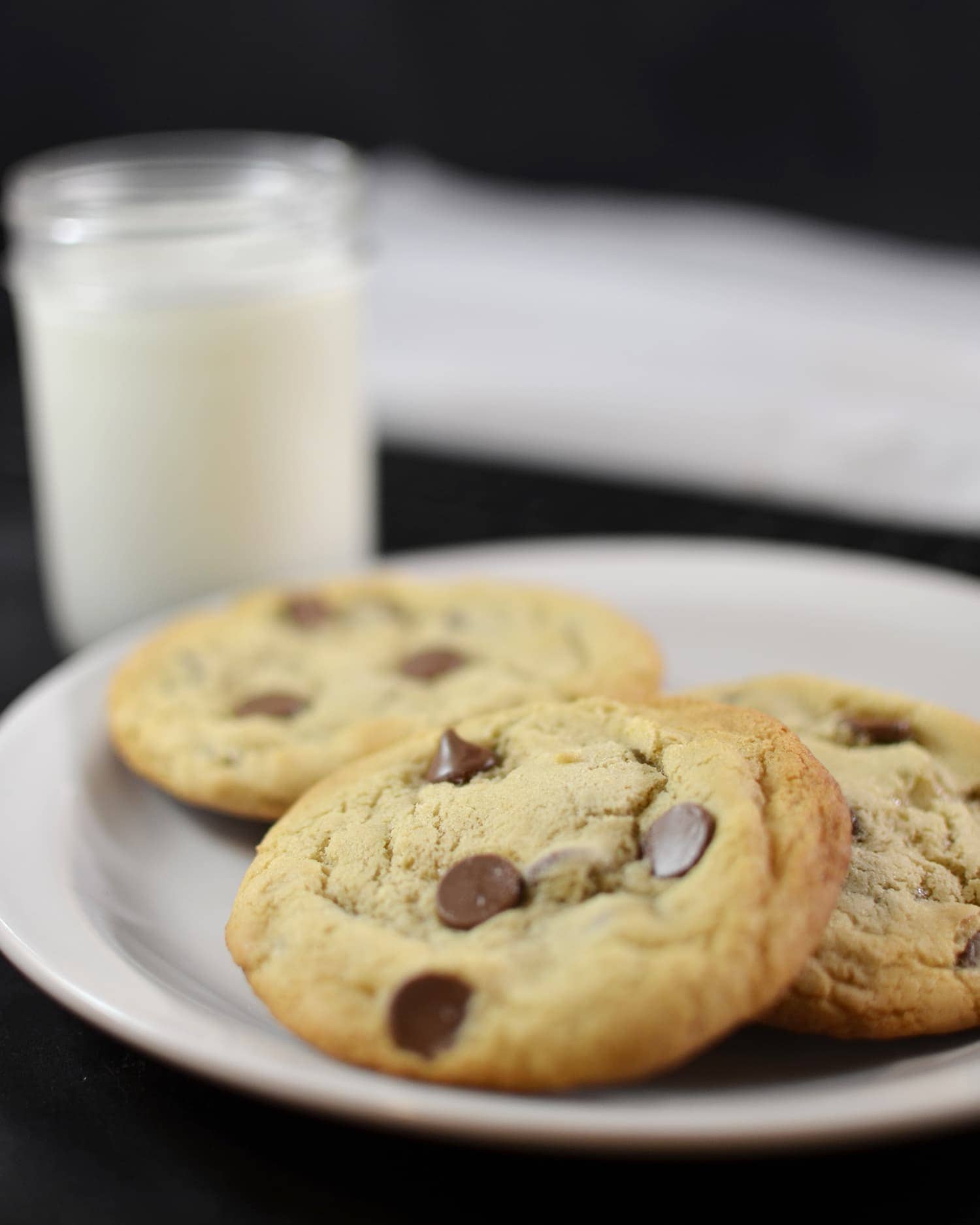 Angled view of chocolate chip cookies on a white plate with milk in the background.