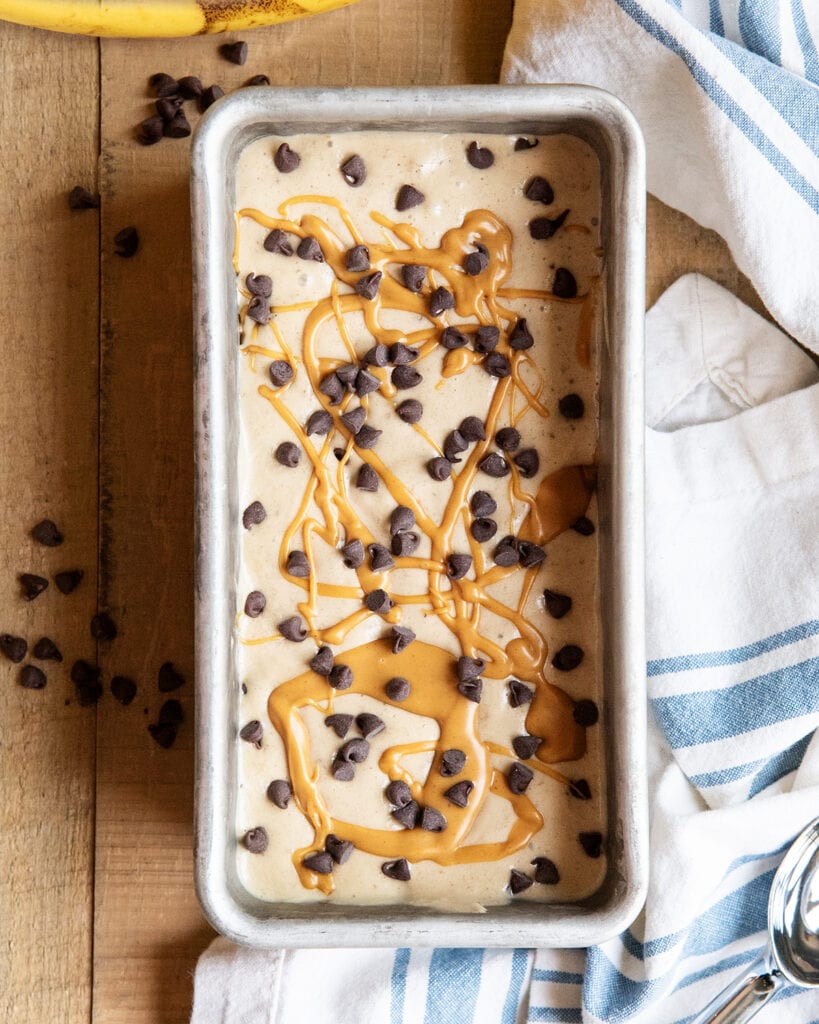 An above view of a pan of healthy banana ice cream topped with mini chocolate chips and peanut butter.