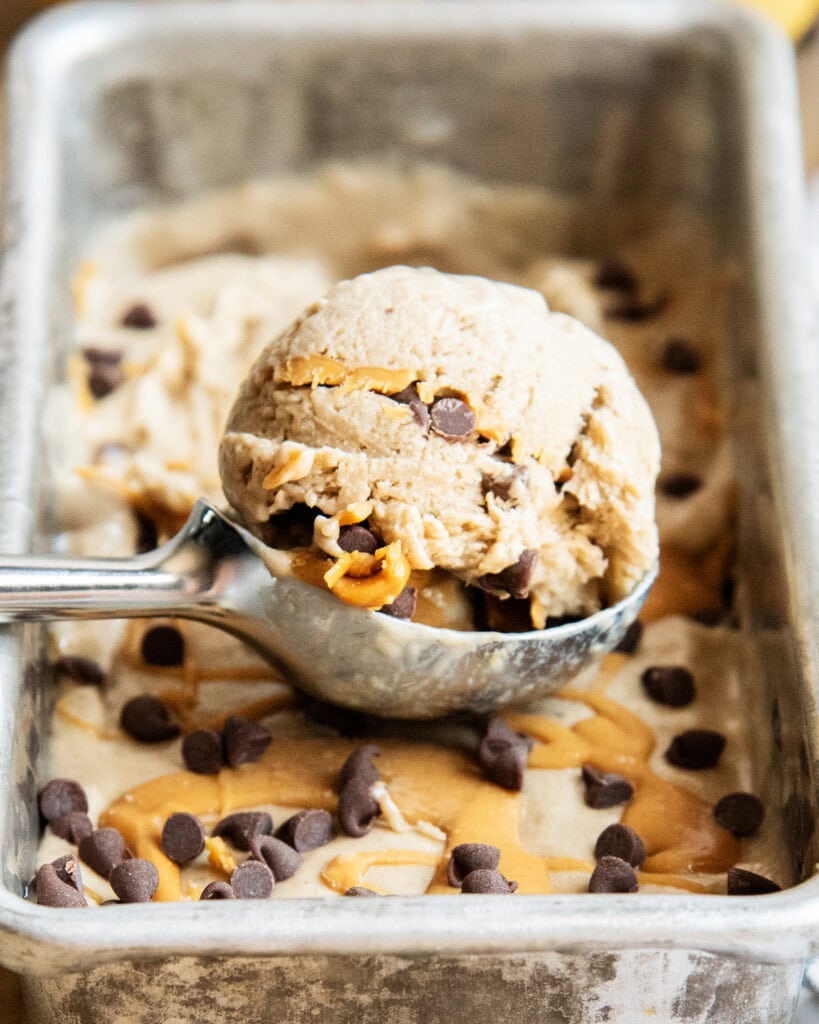 A scoopful of banana ice cream full of swirls of peanut butter in it.