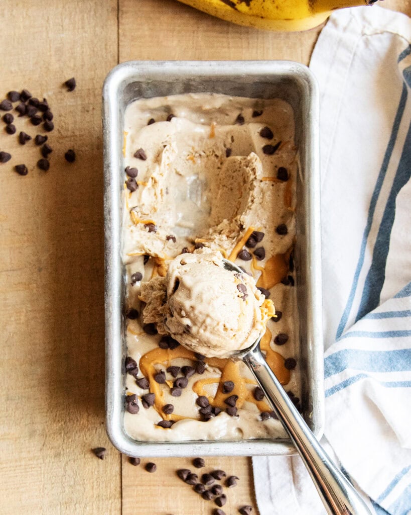 An above view of a pan of healthy banana ice cream topped with mini chocolate chips and peanut butter.