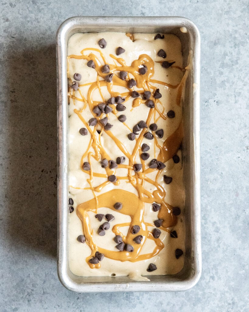 A metal pan full of banana ice cream and topped with swirls of peanut butter and mini chocolate chips.