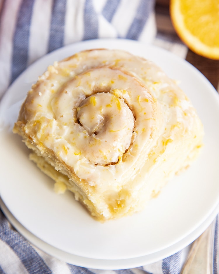 An close up of an orange roll on a white plate, showing the swirls of the roll, and the orange zest filled icing on top.