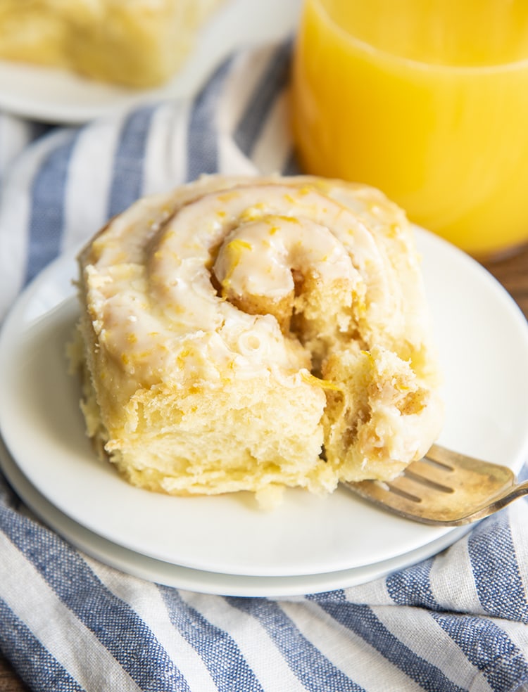 An orange sweet roll on a white plate, with a piece cut out of the roll by a fork.