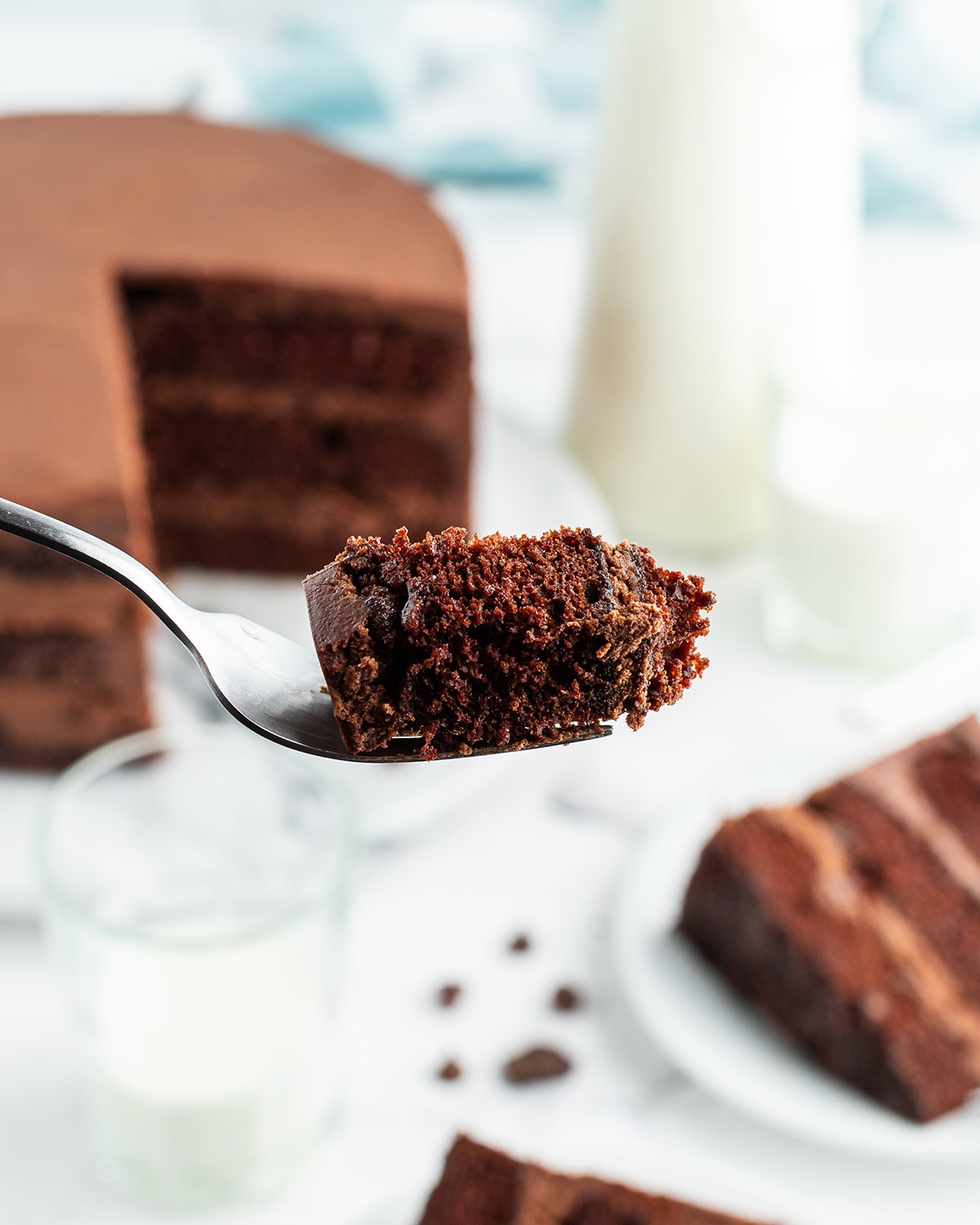 A bite of chocolate cake on a fork with the slice in the background.