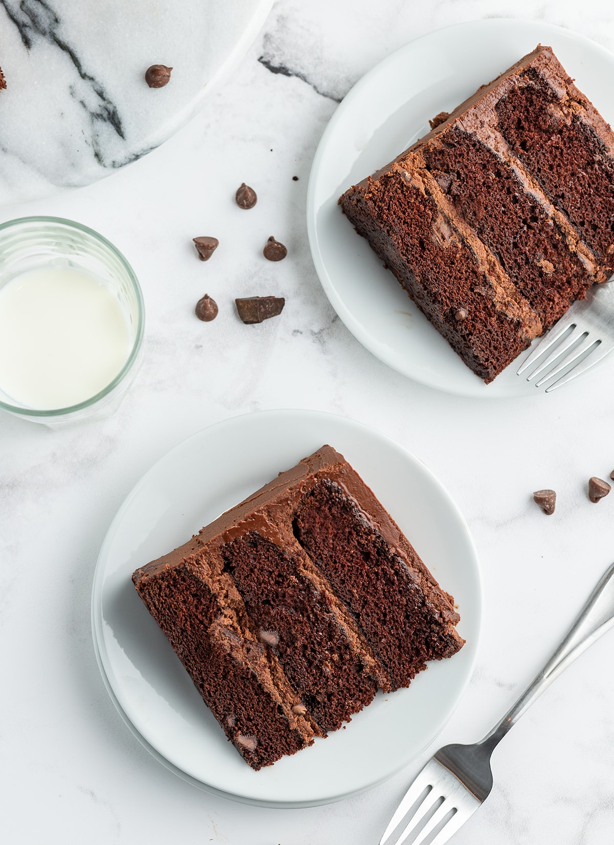 An overhead shot of two three layer chocolate cakes with chocolate frosting on one plates.