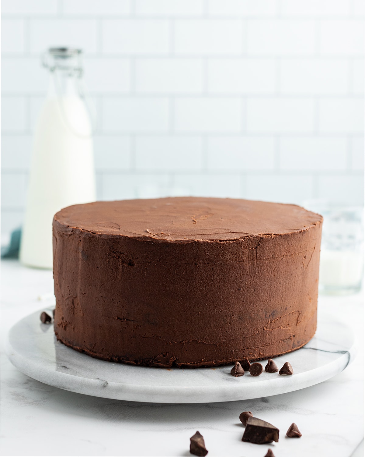 A chocolate cake, plainly frosted with smooth chocolate frosting on a white marble cake turner.