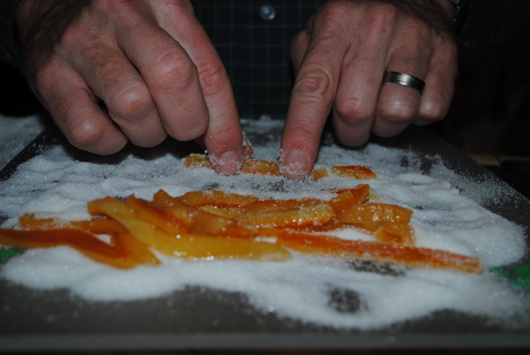 Fried orange peels being rolled in sugar.