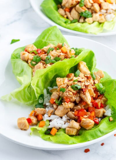 A plate of two chicken lettuce wraps., topped with green onion and red bell pepper.