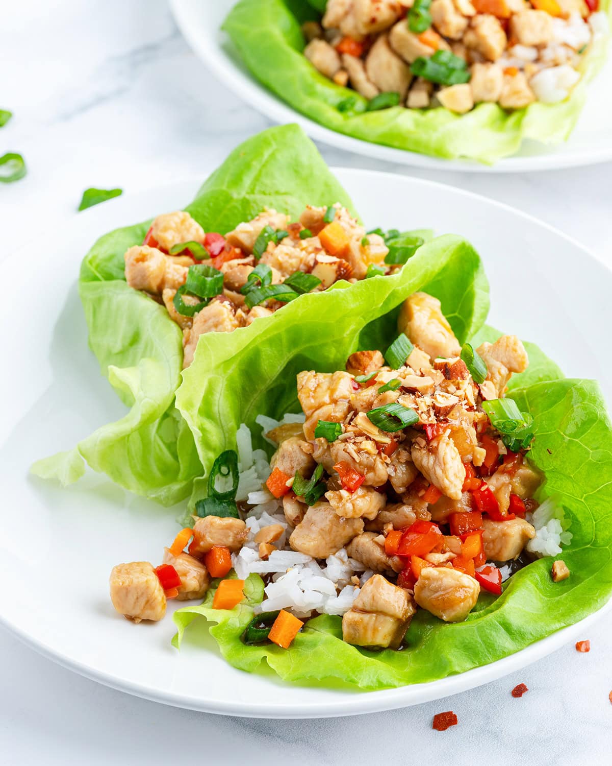 A plate of two chicken lettuce wraps., topped with green onion and red bell pepper.