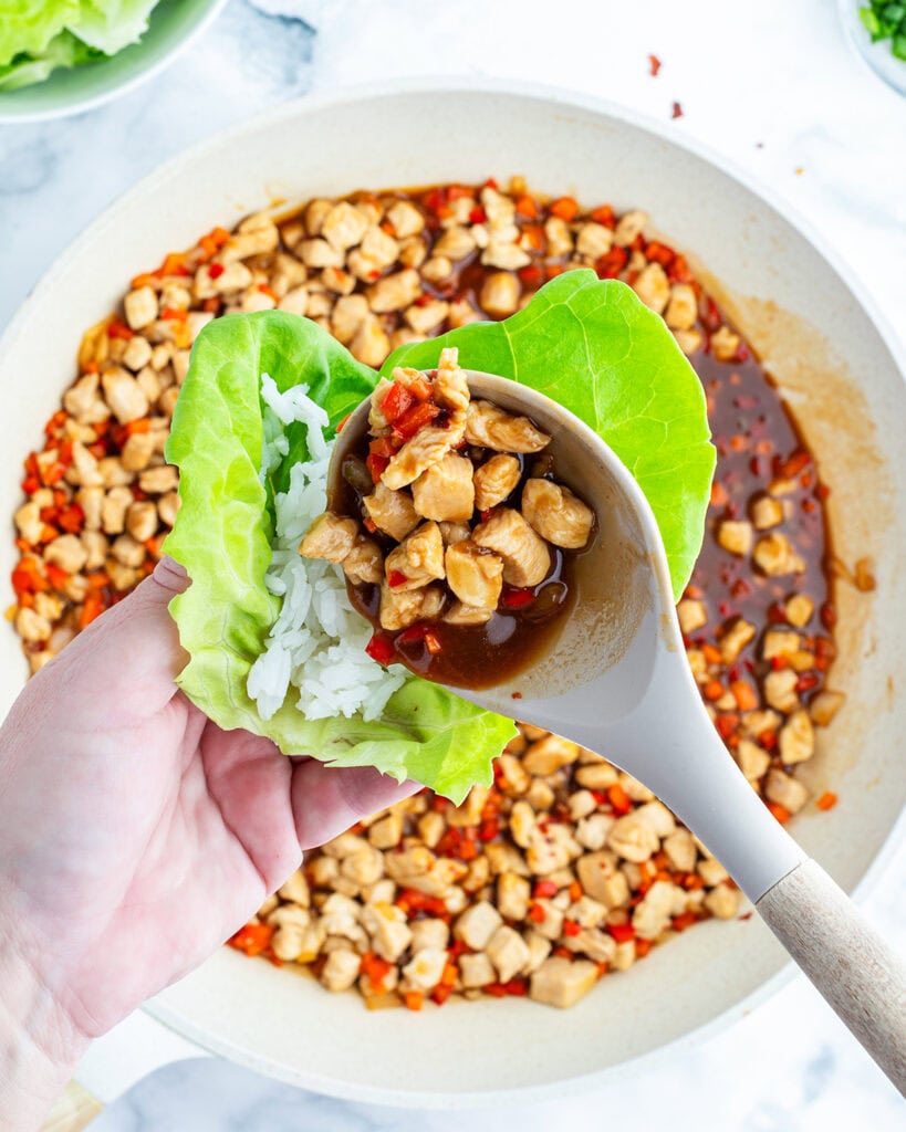 A hand holding a lettuce leaf and inserting the lettuce wrap filling with a spoon.