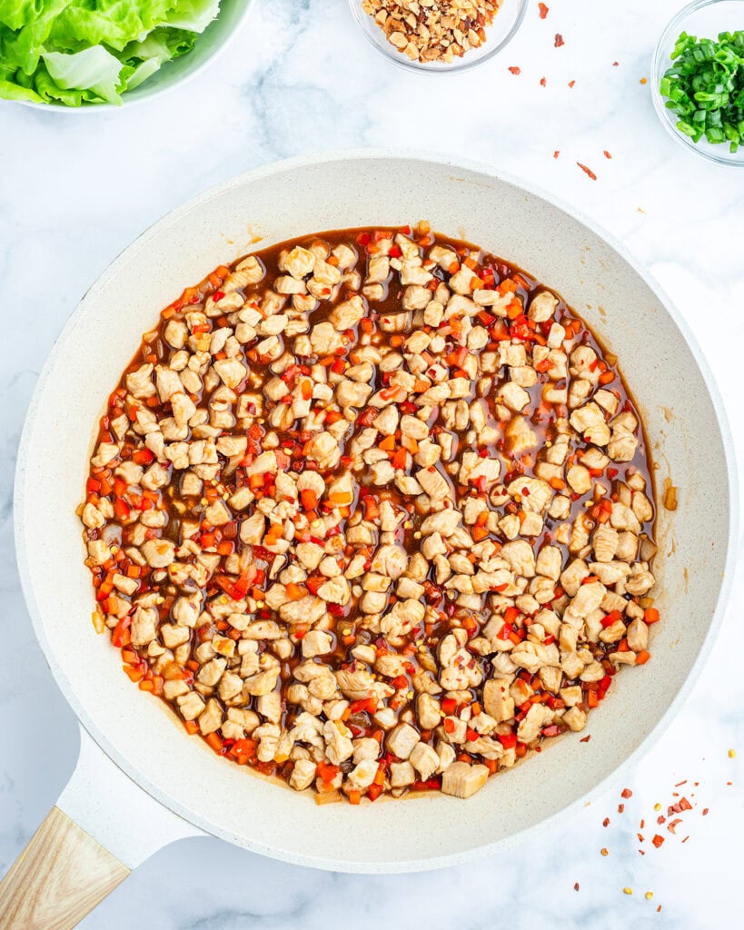 A skillet full of cooked chicken and vegetables in peanut sauce.