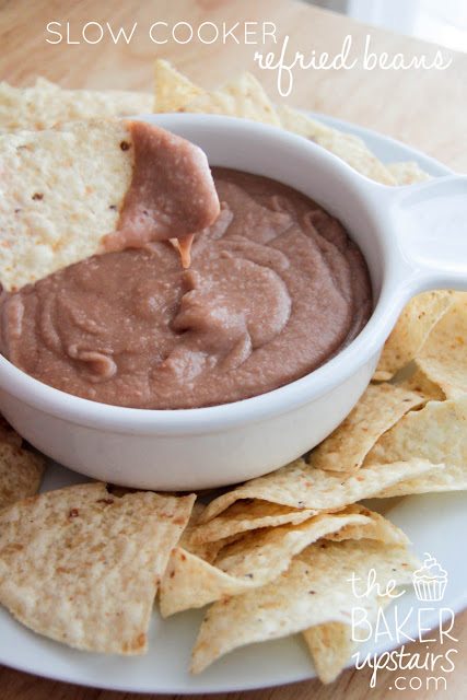 Close up view of a chip dipping into refried beans in a bowl.