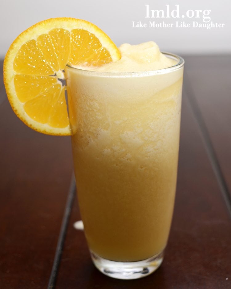 Front view of an orange julius in a glass with an orange on top.