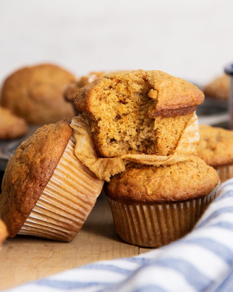A pile of three carrot muffins, and one has a bite out of it.
