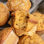 A pile of three carrot muffins, and one has a bite out of it.