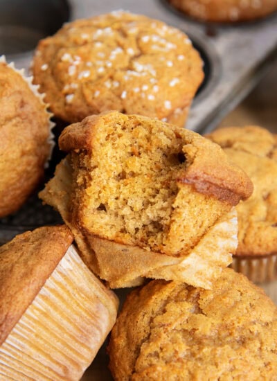 A pile of three carrot muffins, and one has a bite out of it.
