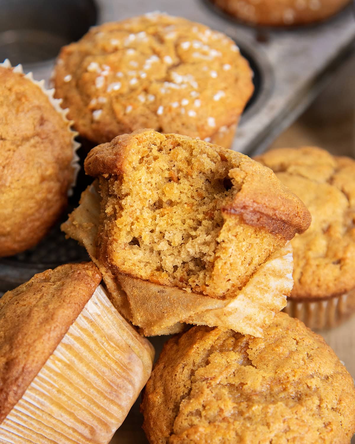 A pile of three carrot muffins, and one has a bite out of it.
