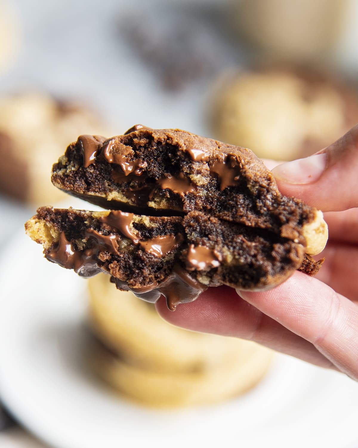 A hand holding two halves of a chocolate marble cookie with melted chocolate chips in the middle.