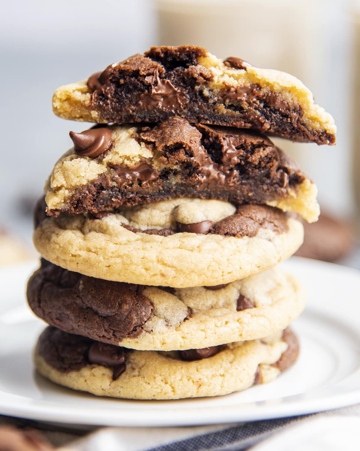 A stack of chocolate chip swirled cookies, with one on top that is cut in half showing the gooey middle of the cookies.