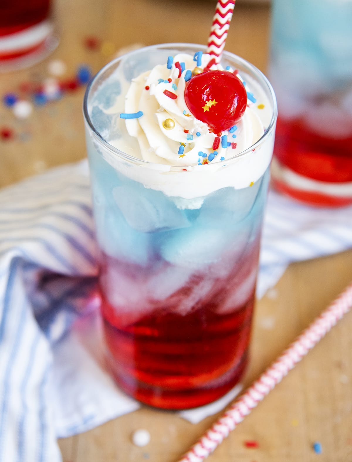 A glass of a half red, half blue drink topped with whipped cream and a cherry.