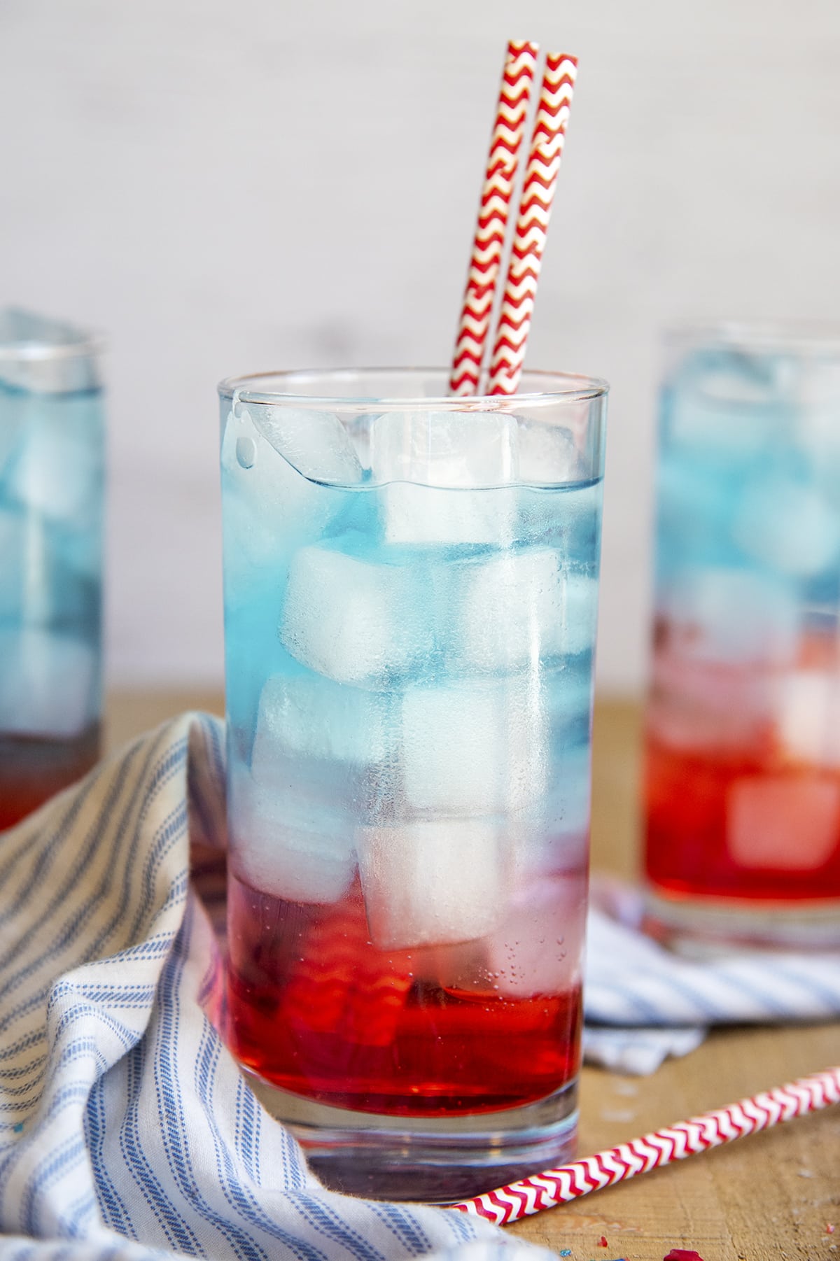 A glass cup full of a red drink on bottom, blue drink on top, and ice throughout the glass.