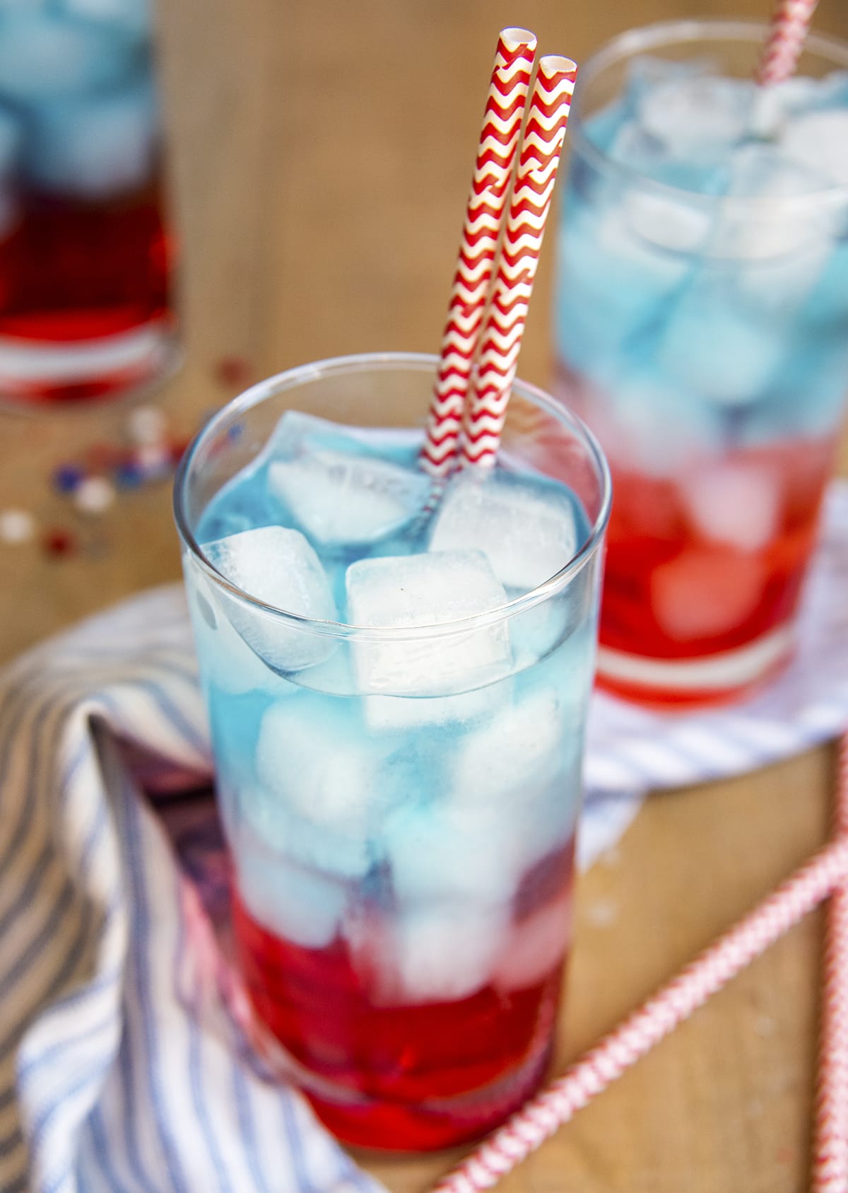 A glass of a red, white, and blue layered drink with two paper straws.