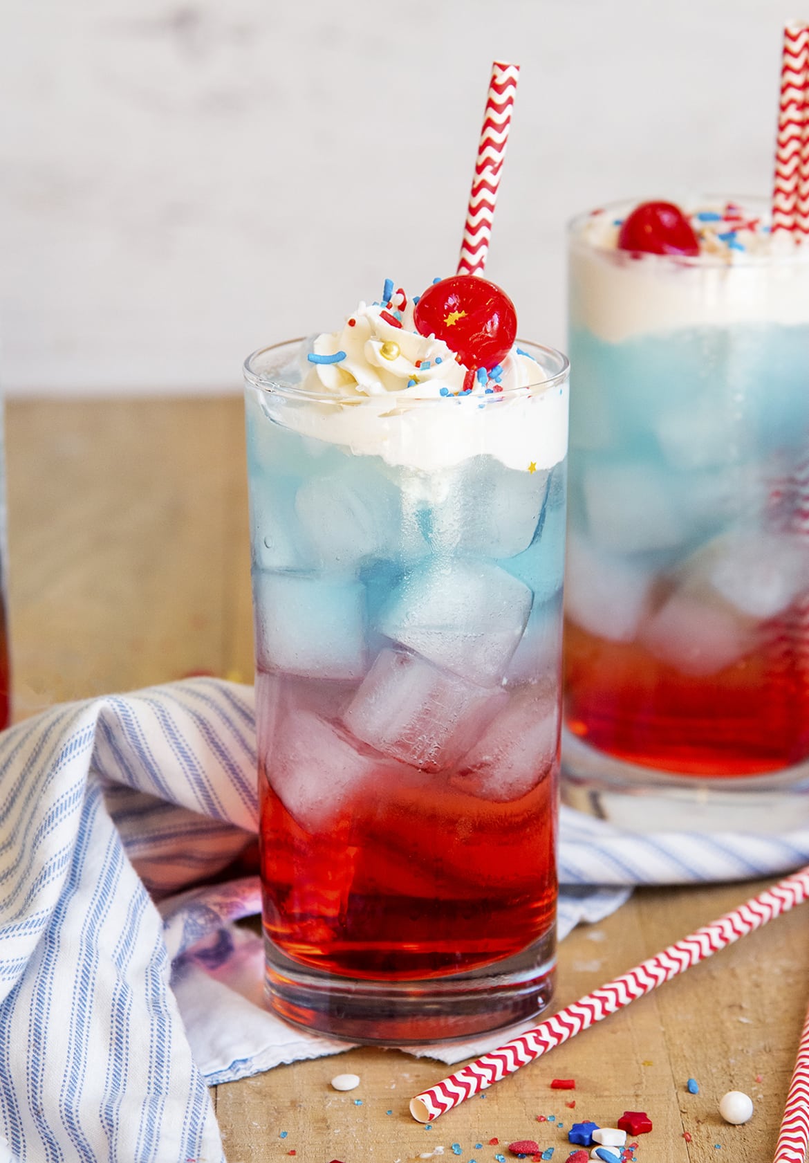 Two glasses of 4th of July layered drinks with whipped cream and cherries on top.