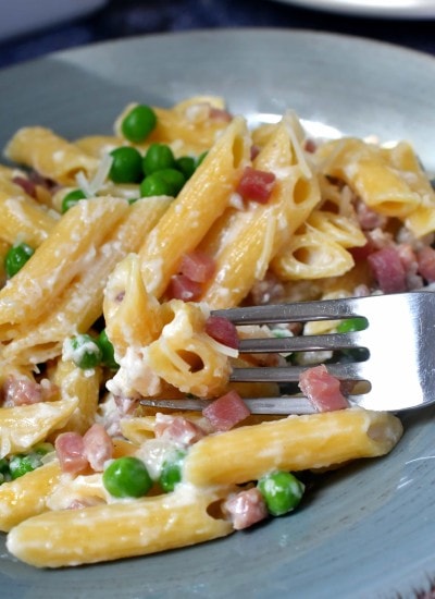 Penne pasta cooked in cream with ham and peas on a blue dish