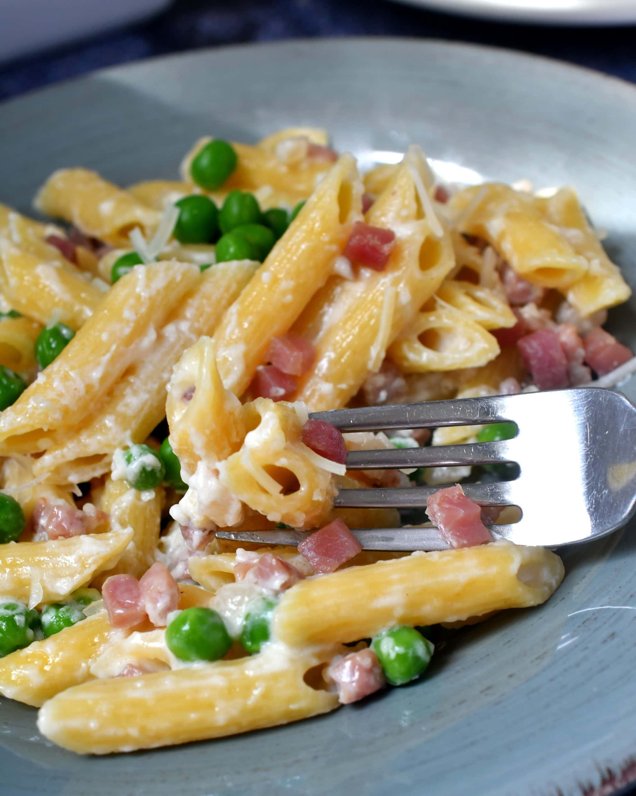Penne pasta cooked in cream with ham and peas on a blue dish