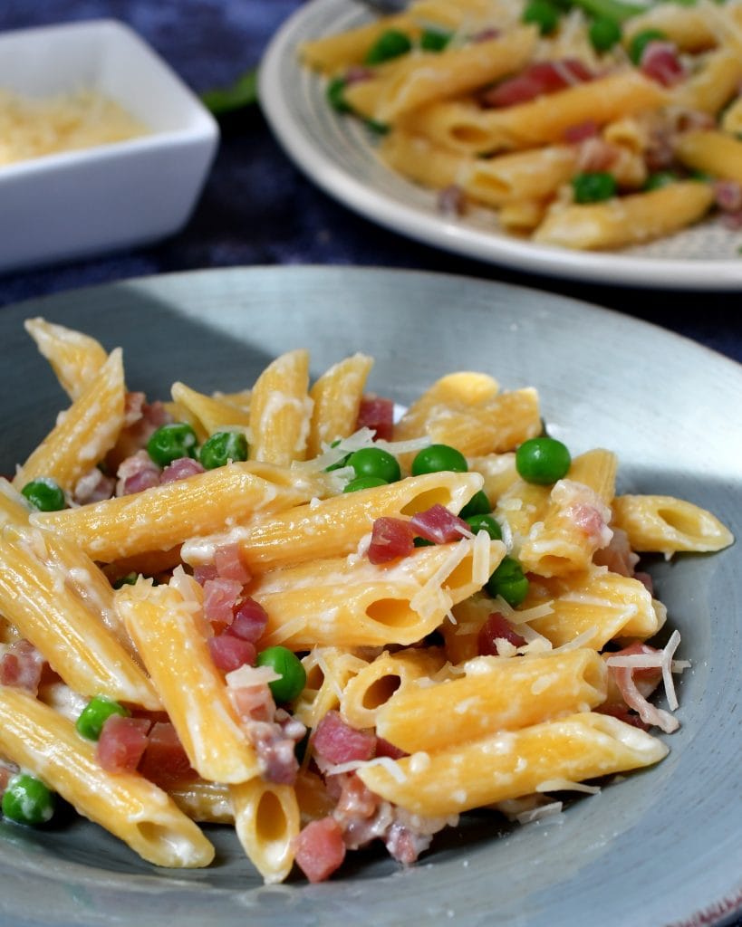 penne pasta with a cream sauce, ham, and green peas served on a blue plate