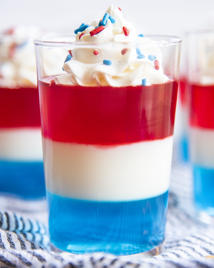 The layers of red white and blue jello served in a small cup topped with fresh whipped cream and red white and blue sprinkles