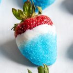 A close up of a fourth of July strawberry dipped in white chocolate and blue sanding sugar.