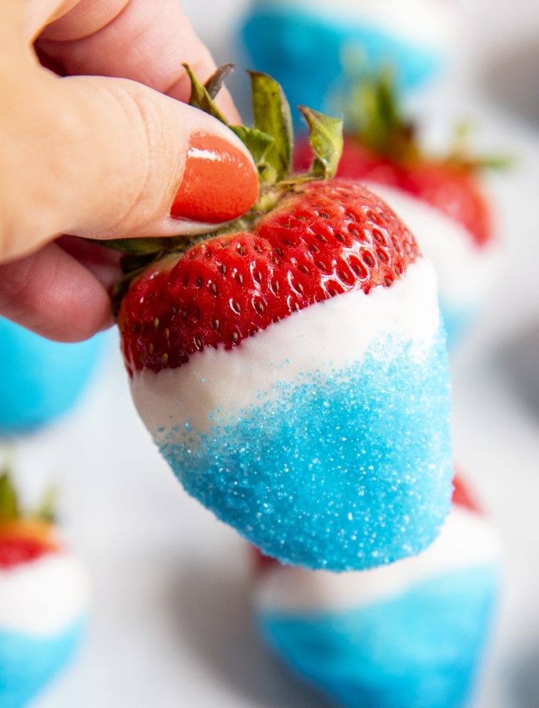A hand holding a white chocolate dipped fourth of July strawberry.