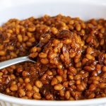 A spoonful of barbecue baked beans above a dish.