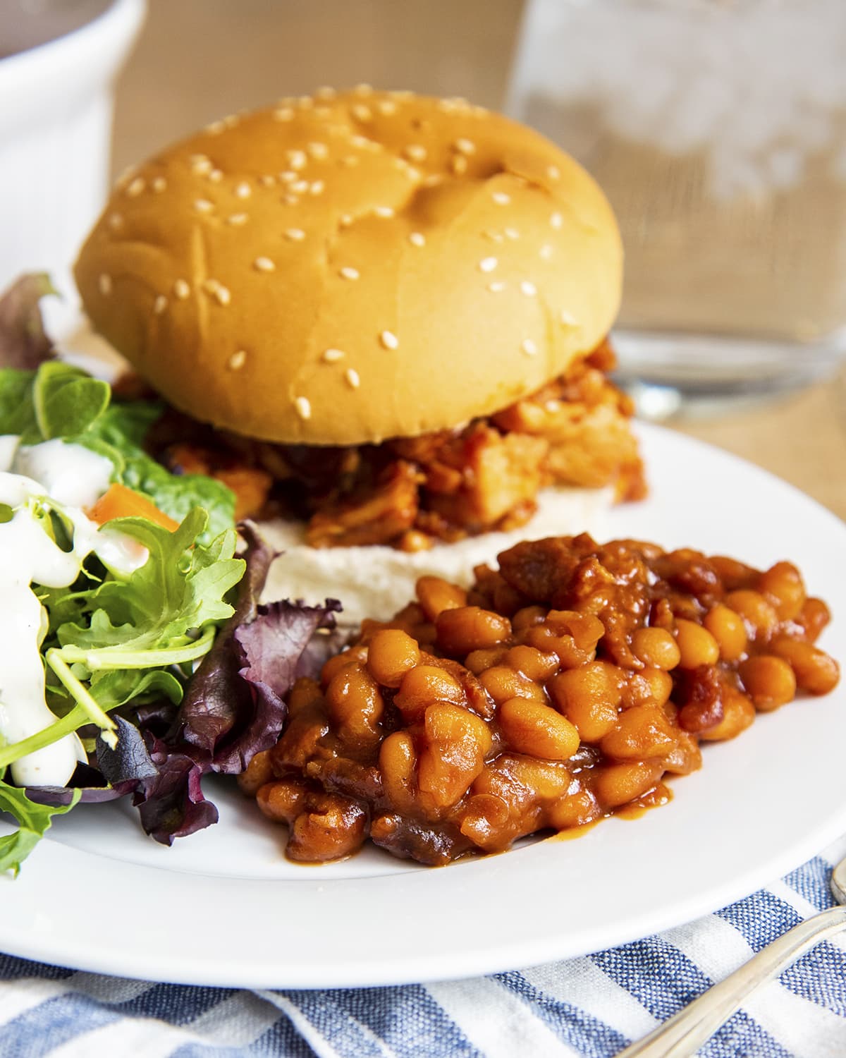 A plate with bbq beans, a bbq chicken sandwich, and salad.