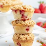 Side image of three stacked bakery style strawberry muffins with crumble on top.