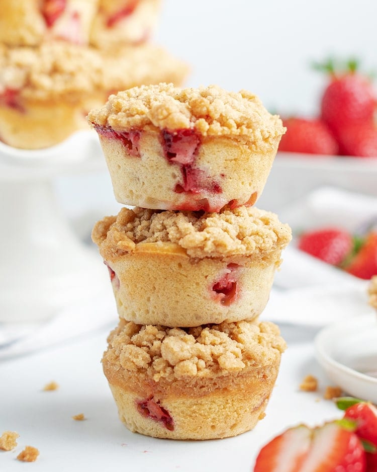 Side image of three stacked bakery style strawberry muffins with crumble on top.