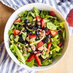 A salad with berries and candied almonds tossed together in a bowl with no dressing.