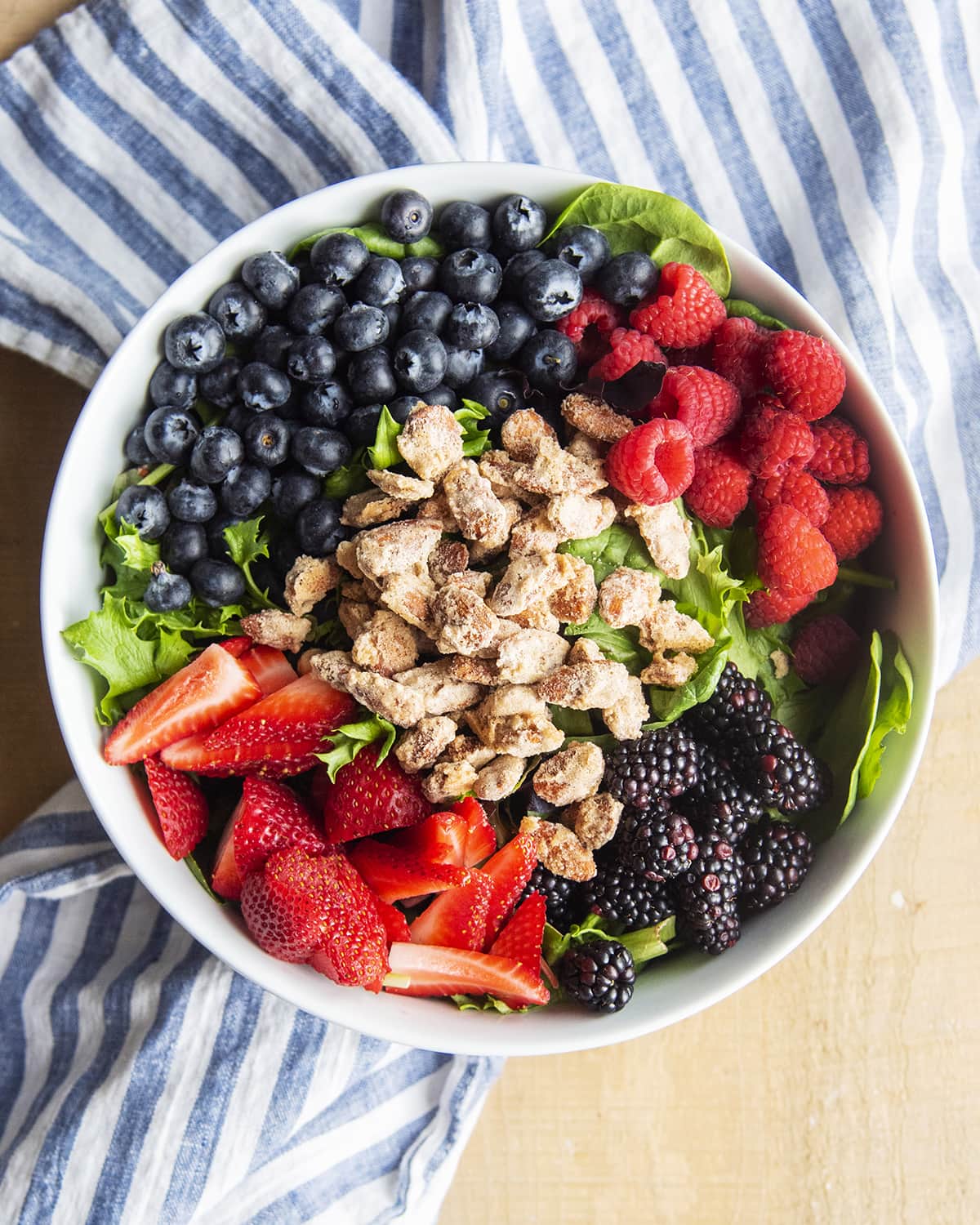 A bowl of lettuce, fresh berries, and candied almonds.