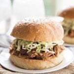A bbq pork sandwich topped with coleslaw on a plate.
