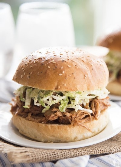 A bbq pork sandwich topped with coleslaw on a plate.