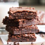 A stack of four double chocolate brownies on baking paper with chocolate chips in front.
