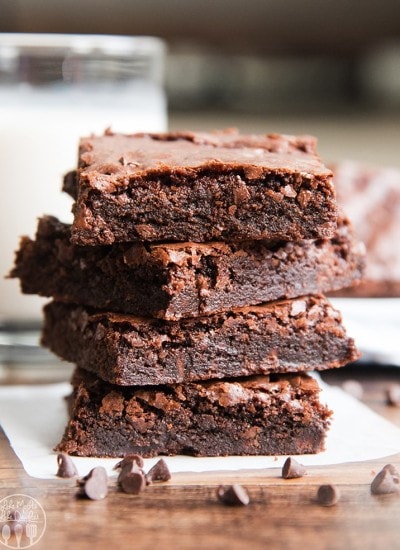 A stack of four double chocolate brownies on baking paper with chocolate chips in front.