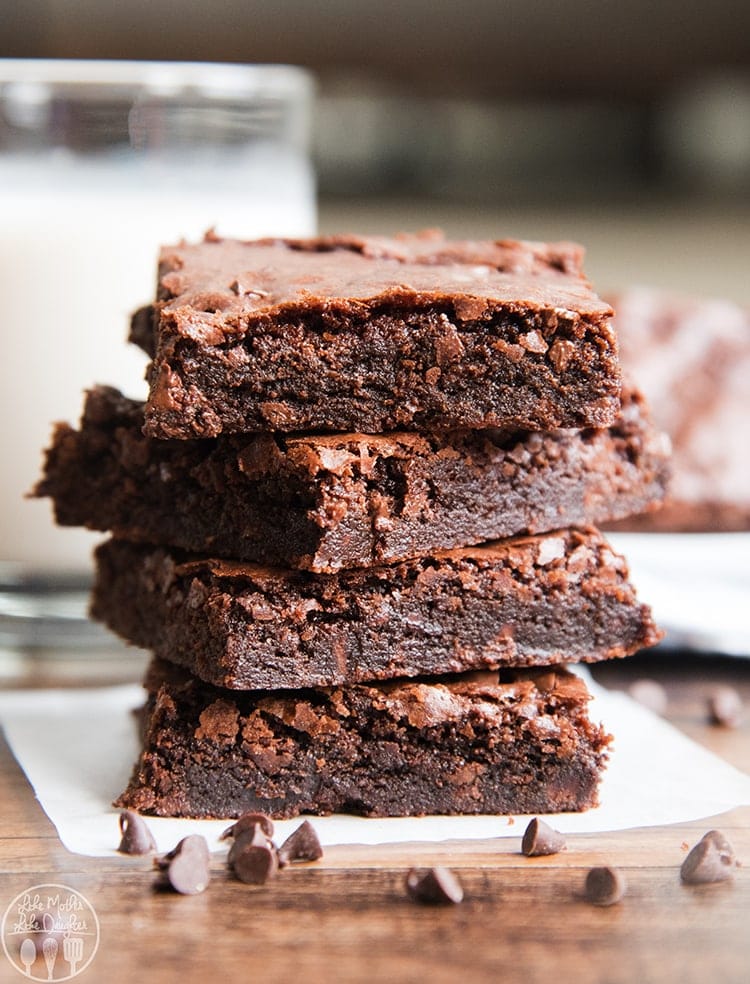 A stack of four double chocolate brownies on baking paper with chocolate chips in front.