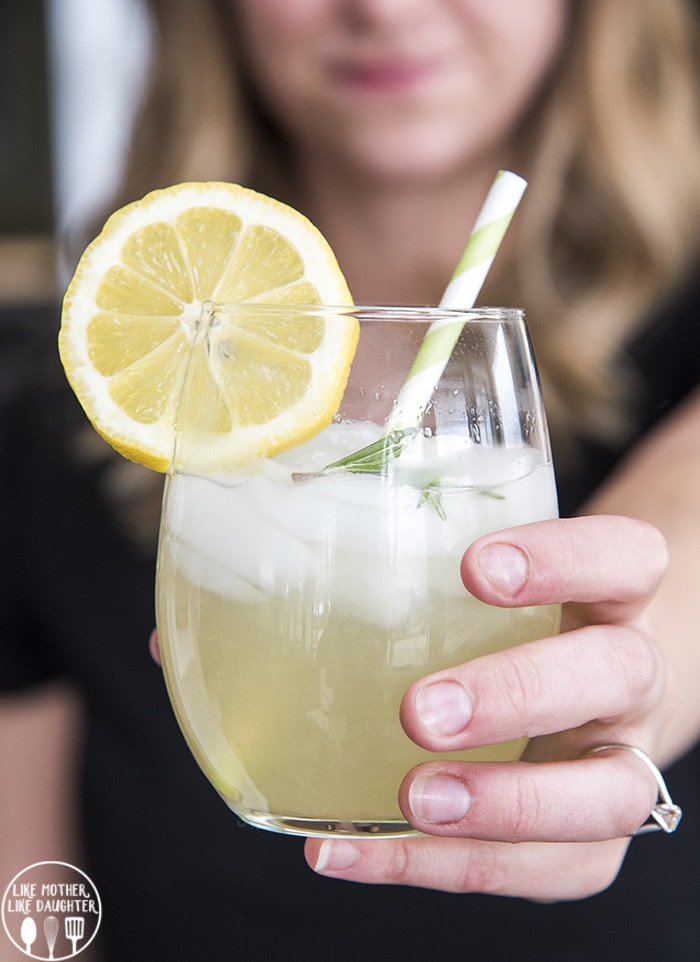 A hand holding a glass of rosemary lemonade.