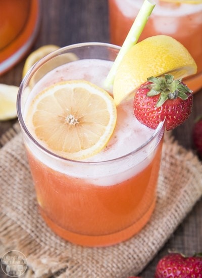 A glass of strawberry lemonade topped with lemon slices and a strawberry on the edge of the glass.