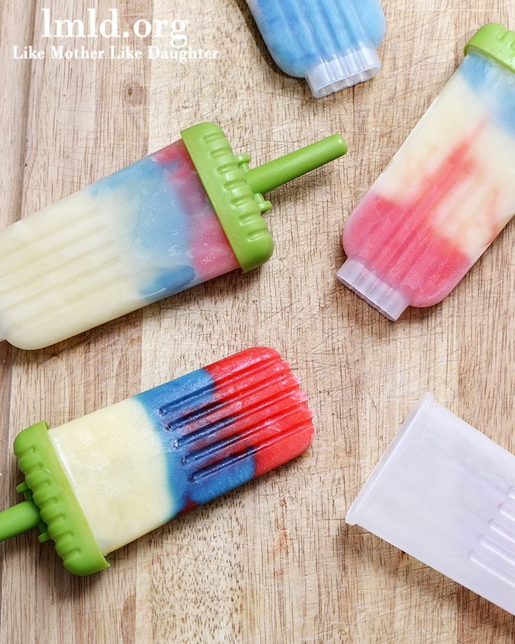 Red white and blue pudding pops on a wood cutting board showing distinct color layers.