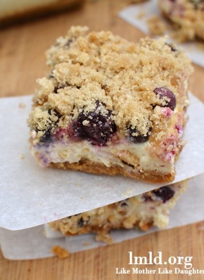 Front view of blueberry and boysenberry lemon cheesecake bar on parchment paper.