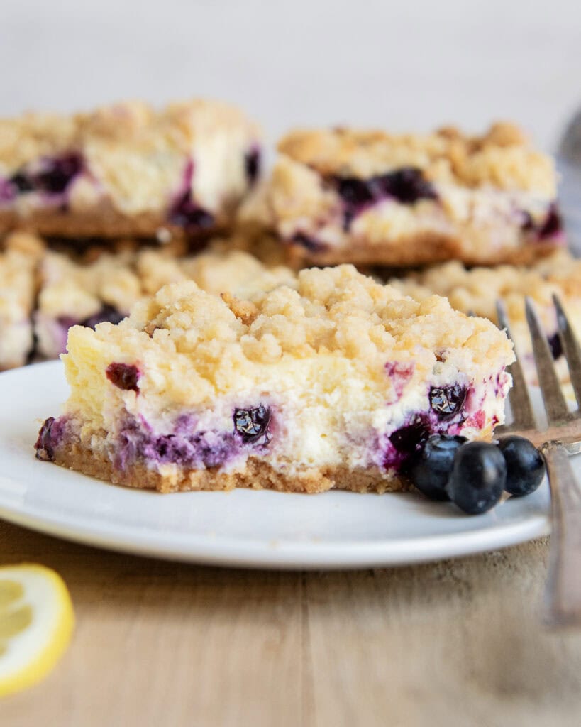 A piece of blueberry lemon cheesecake on a plate with a bite taken out of it.